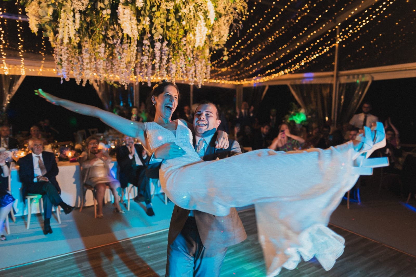 Noivos a rir enquanto o noivo levanta a noiva no colo durante a primeira dança